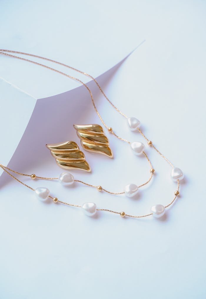 Close-up of elegant gold earrings and pearl necklaces on a minimalist white backdrop.
